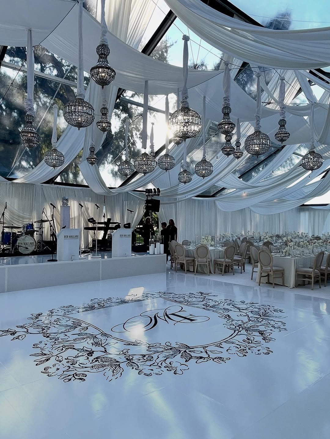 Elegant white dance floor with custom monogram wreath design in a luxury venue with crystal chandeliers - Celebration Creations vinyl dance floor wrap